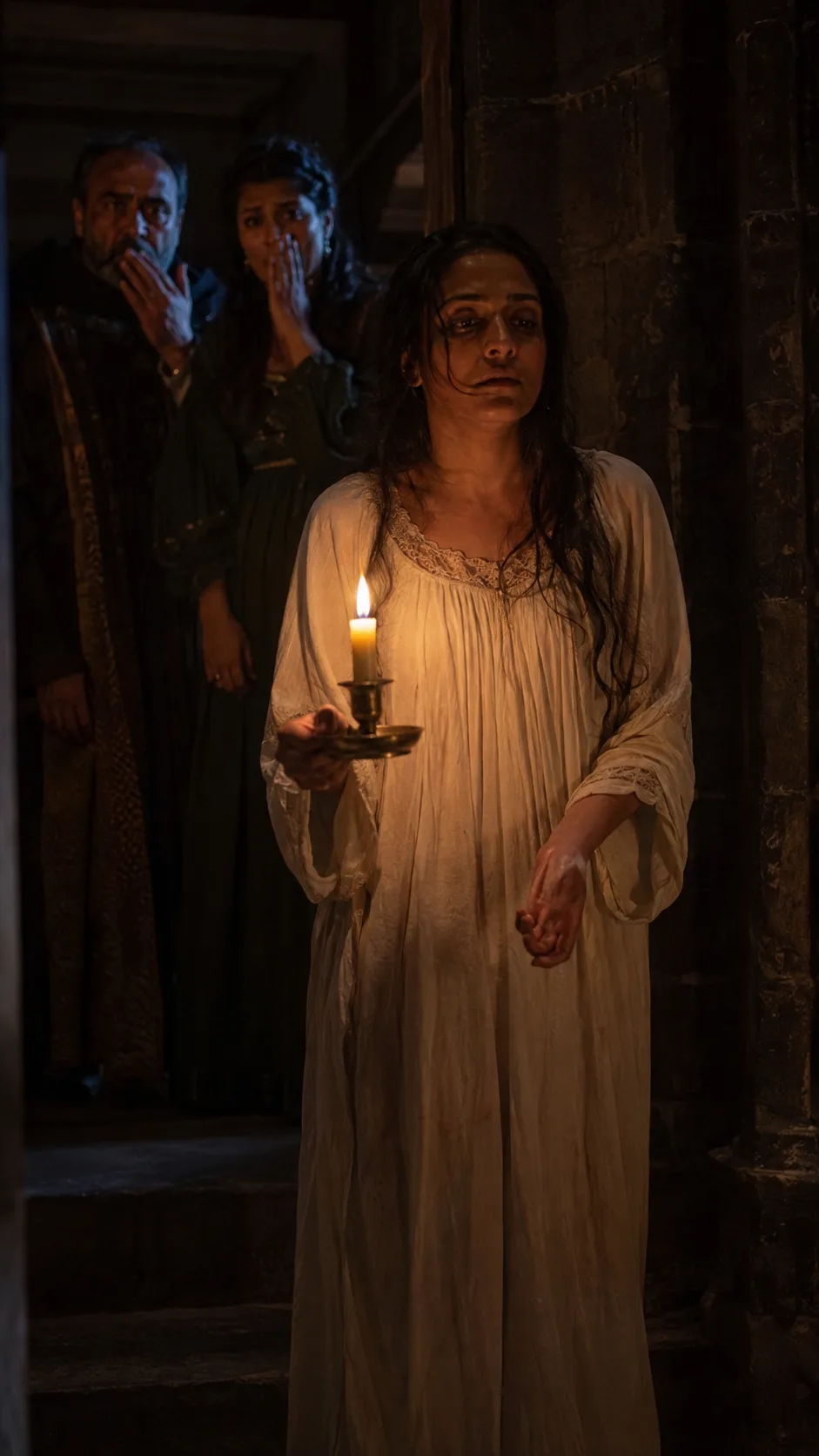 Lady Macbeth, candle in hand, sleepwalks through the dark castle wringing her hands as if washing away an invisible stain, watched in horror by a doctor and gentlewoman.